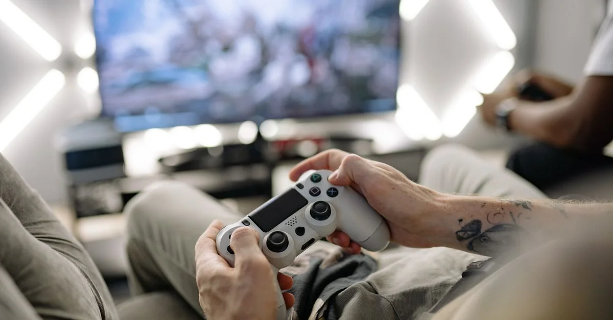 Mains tenant une manette de jeu vidéo dans un salon moderne, jouant à la télévision.