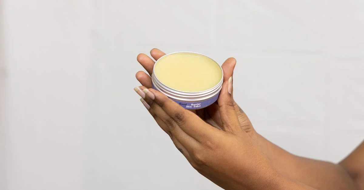 Gros plan sur des mains tenant un pot de crème hydratante sur fond neutre, mettant l'accent sur les soins de la peau.